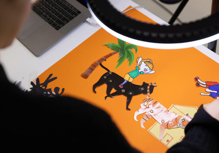 A table with an orange piece of paper has some printed and cut out animated animals which are being arranged, under a bright light. 