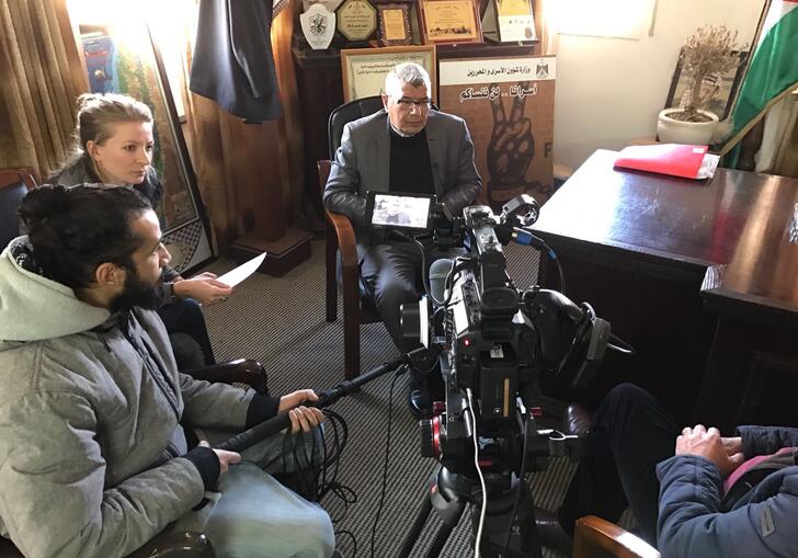 A group of people sit in a room in front of a camera during an interview.