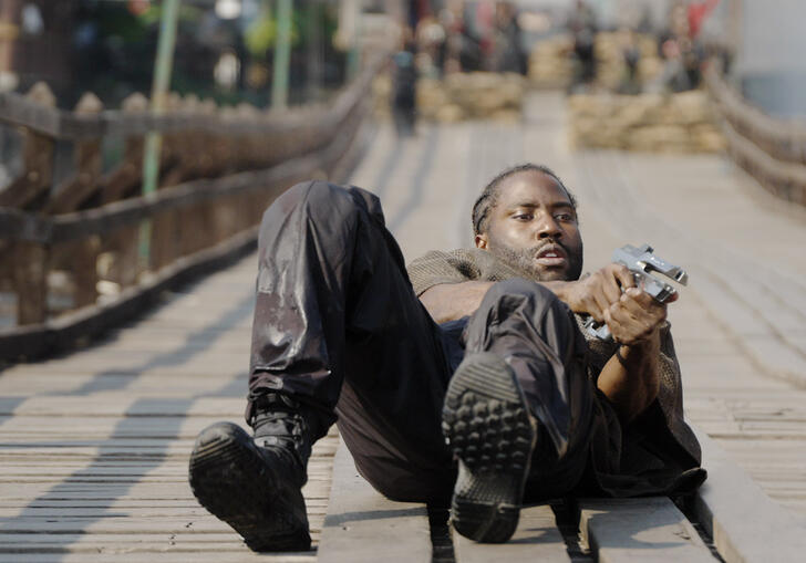 A soldier holds a gun in his hand whilst lying on the floor, ready to shoot. 