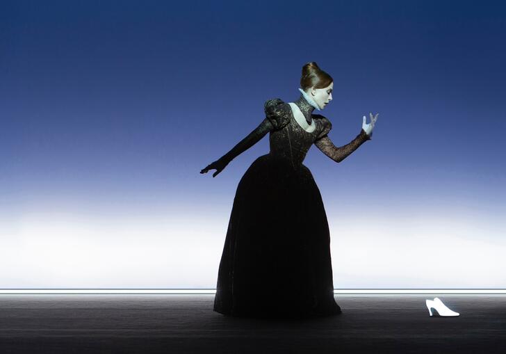 A performer dressed as Mary Stuart in an old-fashioned gown. They look to their left-hand side towards a white shoe.