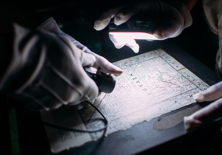Two pairs of hands wearing white gloves move a camera over a map.