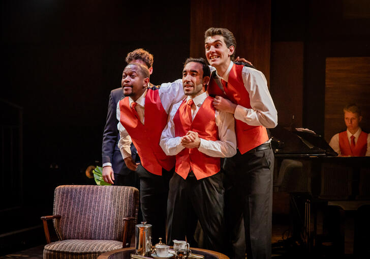 Three singers in red waistcoats, with grand piano in background