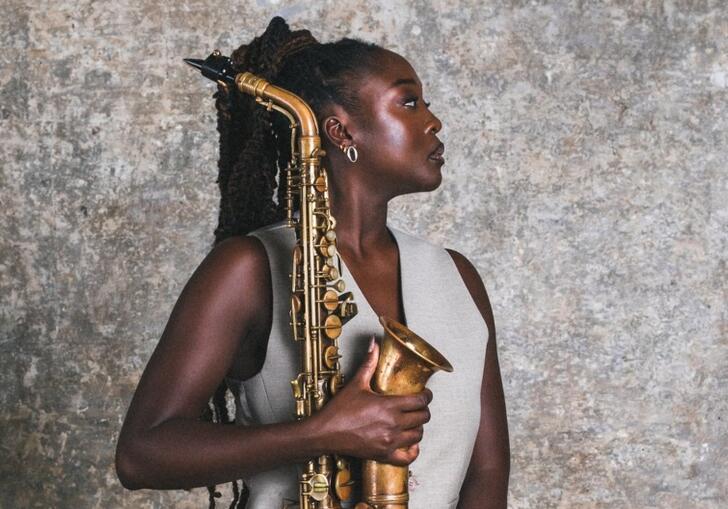 A woman sitting in profile with dark, braided hair holding her saxophone
