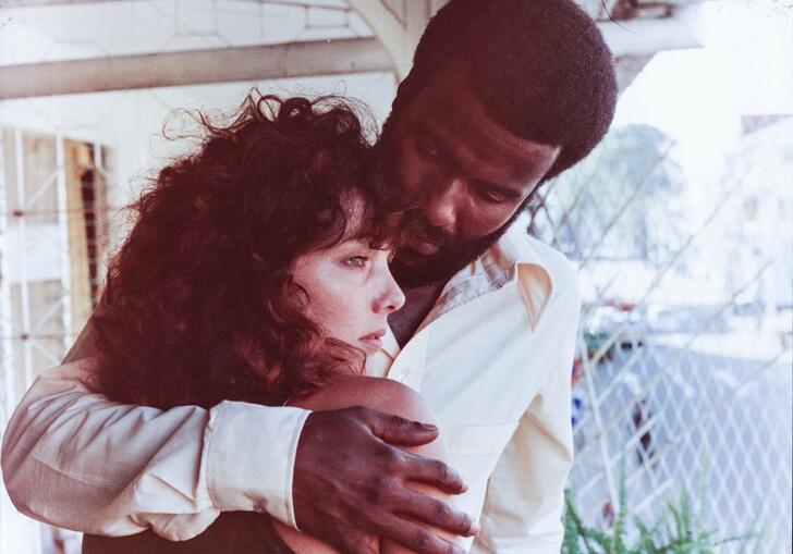 A man holds a woman whilst she looks out on a porch. 