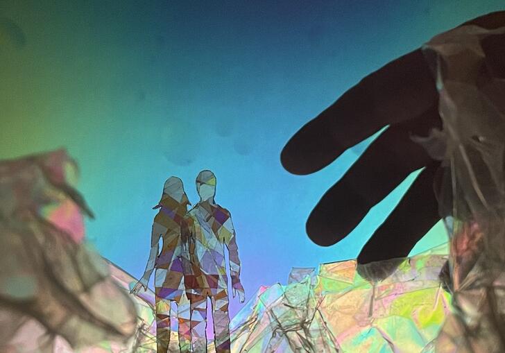 Two people crafted out of see through material stand before each other in a dream-like world. A hand reaches towards them.