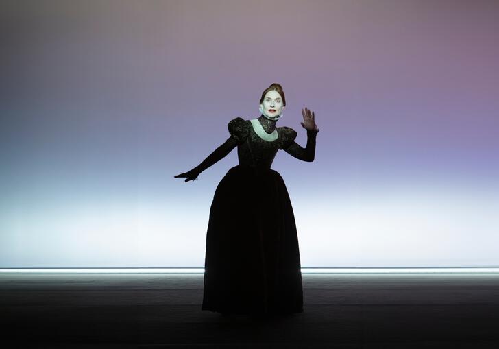 Actress Isabelle Huppert poses as Mary Stuart in an old-fashioned gown against a purple background. 