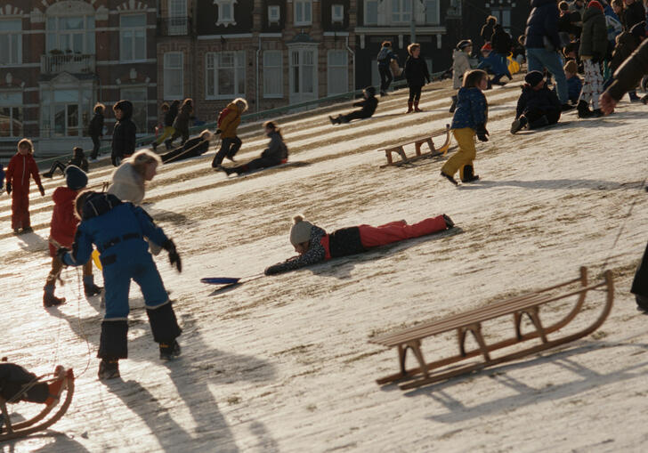 Kids slide down an icey slope with toboggans on a sunny winters' day.