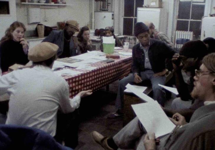 A group of Black and Irish activists sit around a table talking. 