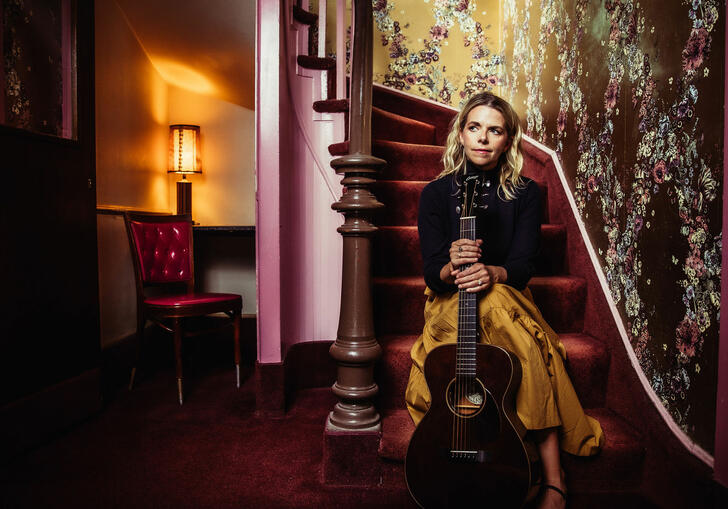 Aoife O'Donovan sits on purple staircase holding guitar