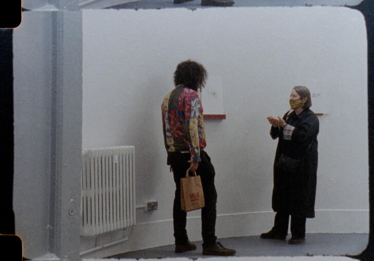 Two people stand talking in a gallery. 