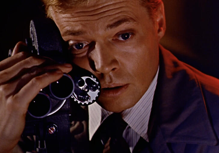 A man holds a film camera to his face and gazes dreamily forward.