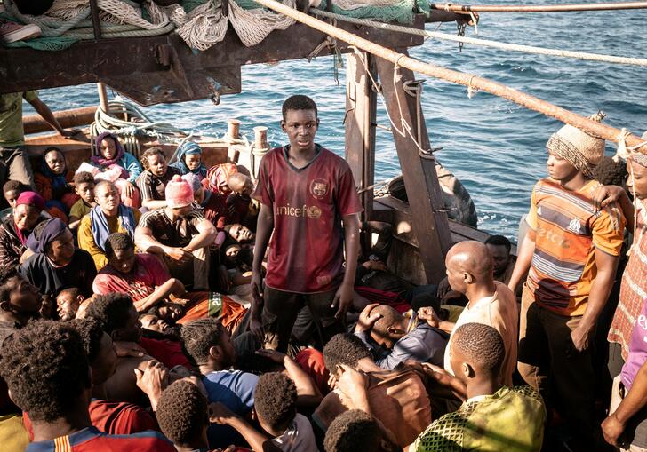 A young man in a football shirt stands on a boat full of people.