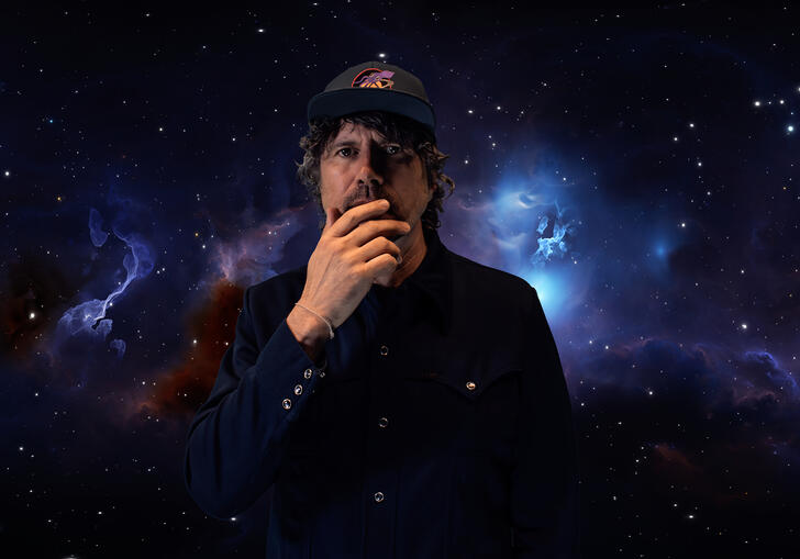 Gruff Rhys stands, hand over mouth in front of galaxy backgrounds