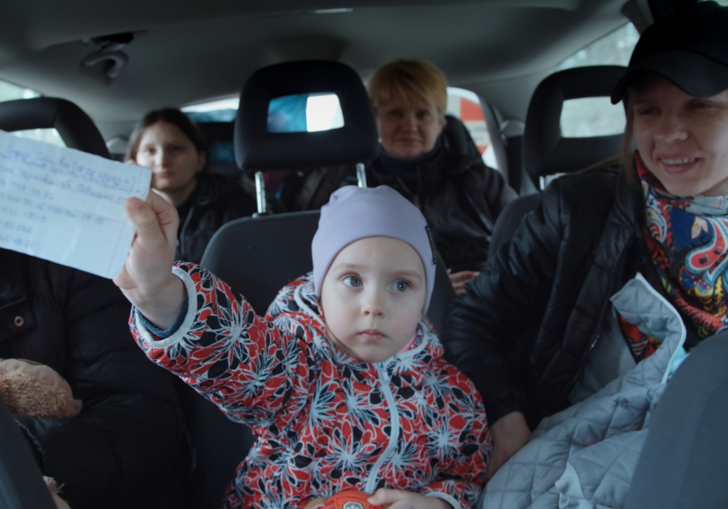 A young girl sitting in a van full of people holds up a note.