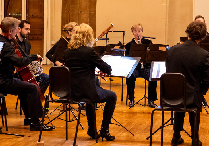 A small selection of musicians from Britten Sinfonia seated in a semi-circle, playing their instruments