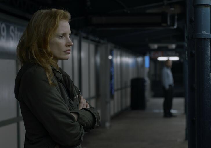 A woman stands on a train platform in the dark, looking concerned.