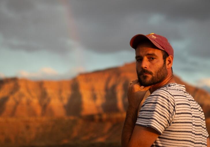 Roo Panes looks over his shoulder at the camera, surrounded by a rugged landscape