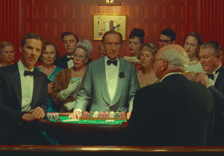A group of well dressed men stand around a gambling board in a casino, looking forward.