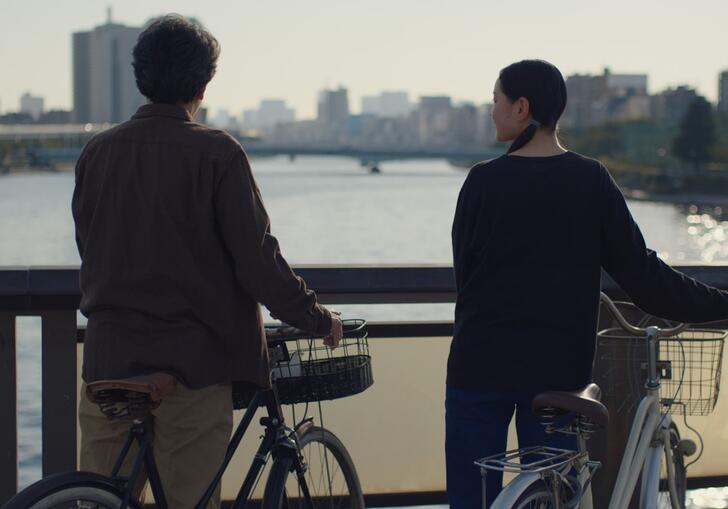 Two people stand with bicycles on a bridge looking out over a river