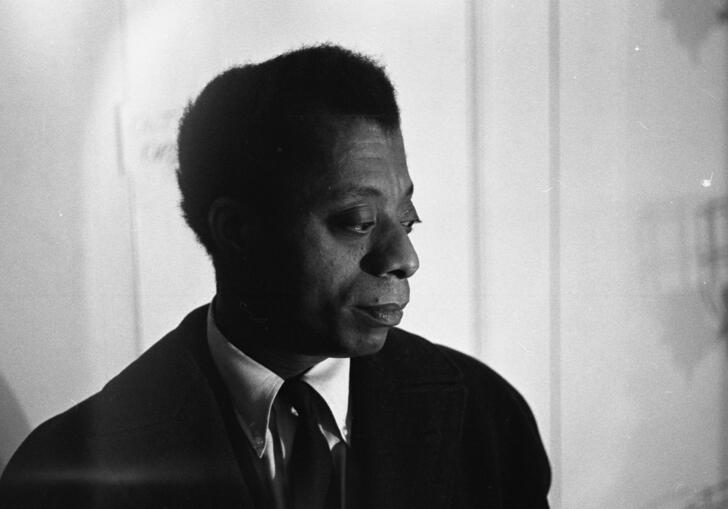 James Baldwin, wearing a suit, looks thoughtfully to the side. 