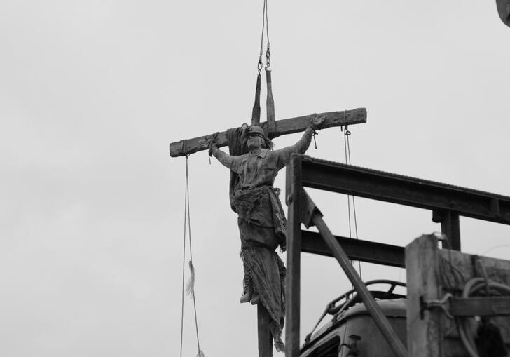 A statue of a saint on a crucifix hangs over a dark sky.