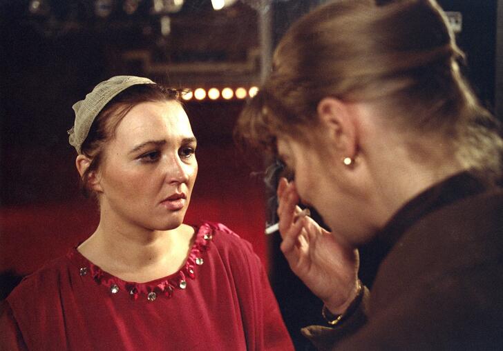 A woman looks on as another woman cries in front of her. 