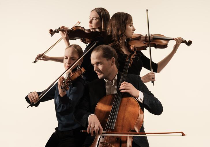 The Dudok Quartet playing their instruments. They are positioned in a close huddle, each person facing a different direction. They are against a cream coloured background.