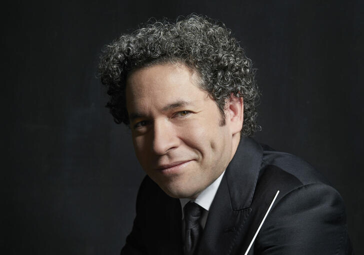 Headshot of Gustavo Dudamel smiling at the camera while holding his baton.