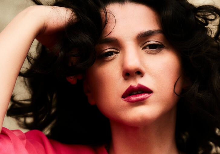 Khatia Buniatishvili wearing a coral pink dress, resting her head on her hand