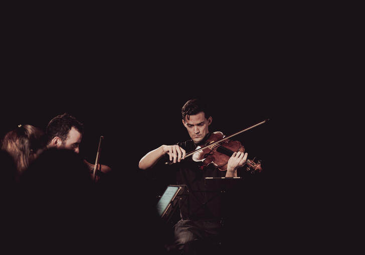 Photo of Stephen Upshaw playing his viola in a darkly lit room