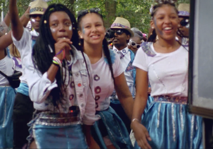 A group of excited young women walk down a street, wearing blue skirts.