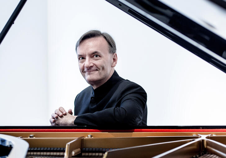 Stephen Hough sitting at a grand piano, smiling at the camera