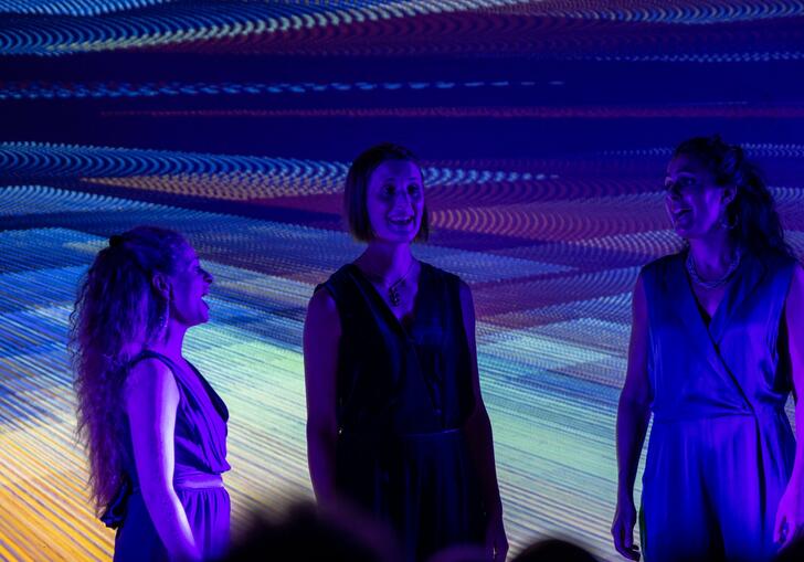 The three members of Voice Trio singing on stage, with purple lights and a purple projection behind them