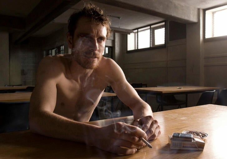 An emaciated man sits in a jail cafe smoking a cigarette. 