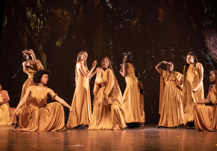 The cast of The Golden Stool performing on stage, wearing long golden dresses