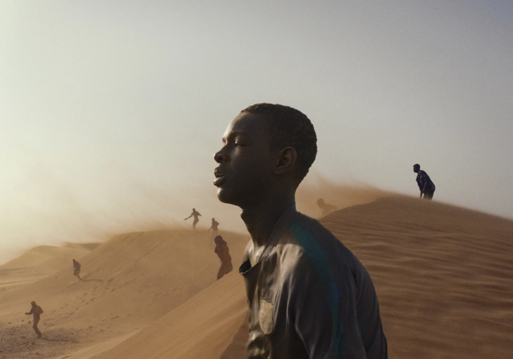 A young, tired man looks ahead in the desert, in the glaring sun. 