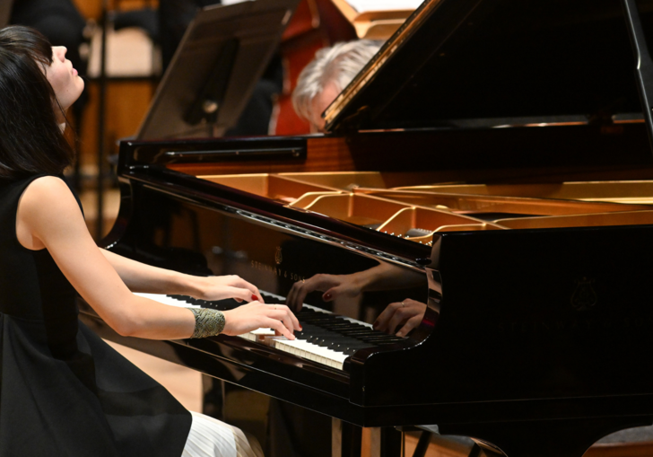 Pianist Alice Sara Ott performing on the Barbican Hall stage. She has short black hair and is wearing a sleevless black top.