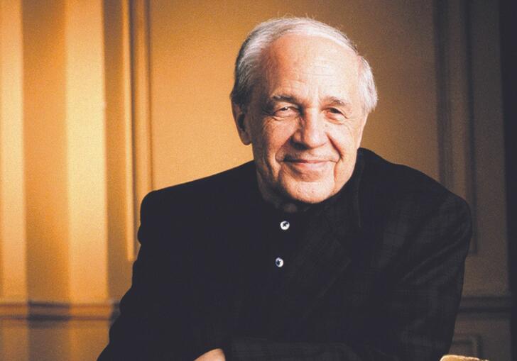 Composer Pierre Boulez sitting down. He is wearing a dark jacket and has white hair.