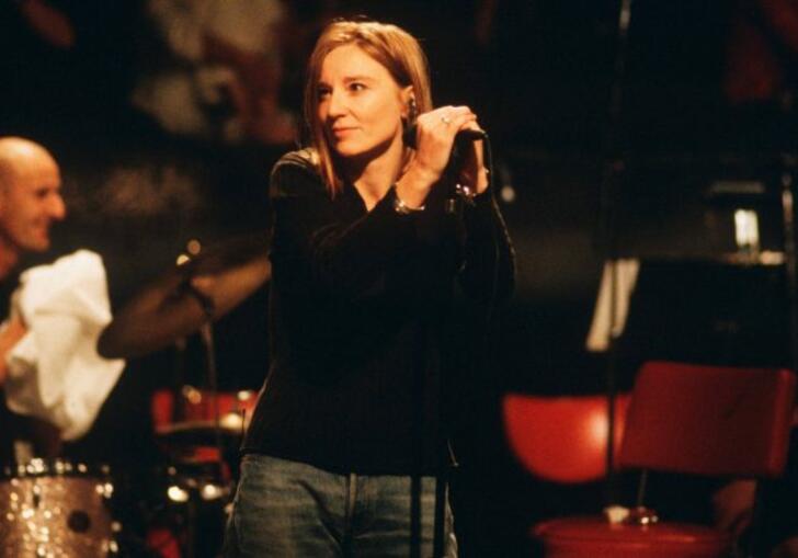 The lead singer of Portishead stands holding the mic.