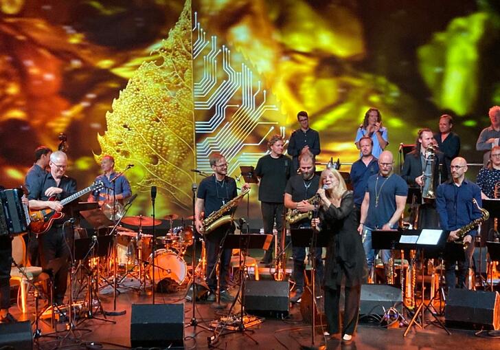 Maria Schneider and Oslo Jazz Ensemble perform on stage, surrounded by orange and yellow lights