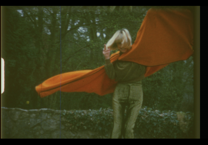 A woman in a large orange cape spins on a roof top. 