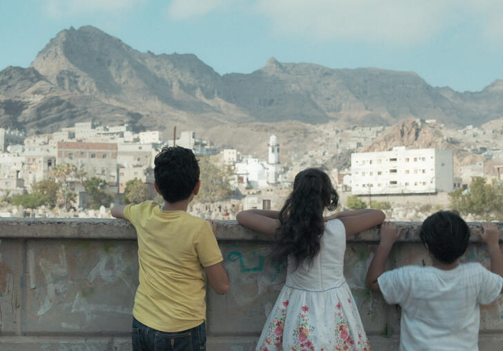 Three young children stand by a wall looking out over a desert city. 