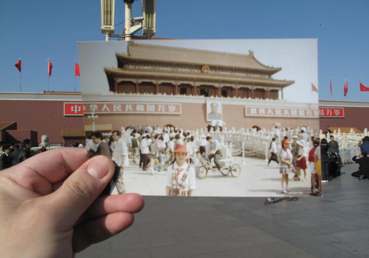 A hand holds a photograph showing a child in uniform standing in Tiananmen Square. Both the earlier photo and person holding the image are stood in the same location.