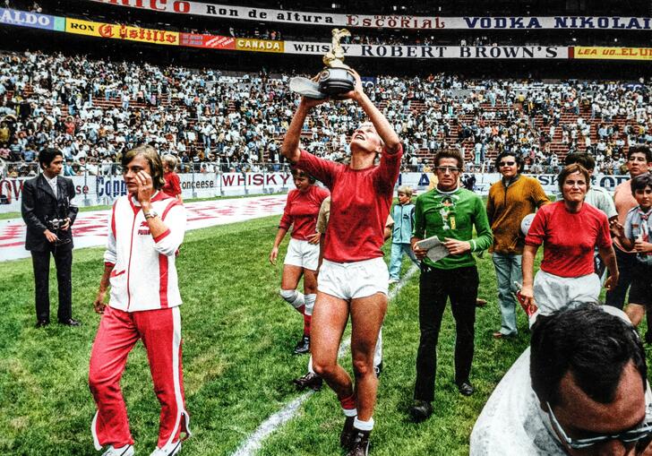 A group of women footballers celebrate in a huge stadium, holding an award cup. 
