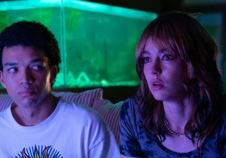 Two young teenagers sit in a dark room facing a TV.