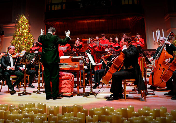 The orchestra performing on stage, surrounded by candles and two Christmas trees