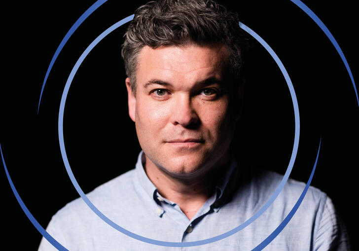 Ryan Wigglesworth facing the camera, with blue circular swirls surrounding him