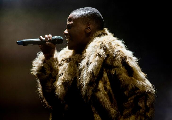 A person in an animal print fur coat sings into a microphone. 