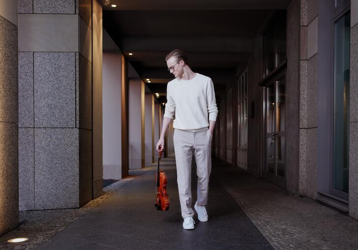 Sao Soulez Lariviere waking down a concrete corridor holding his viola by his side