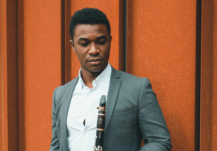 Carlos Ferreira standing with his clarinet against an orange wall